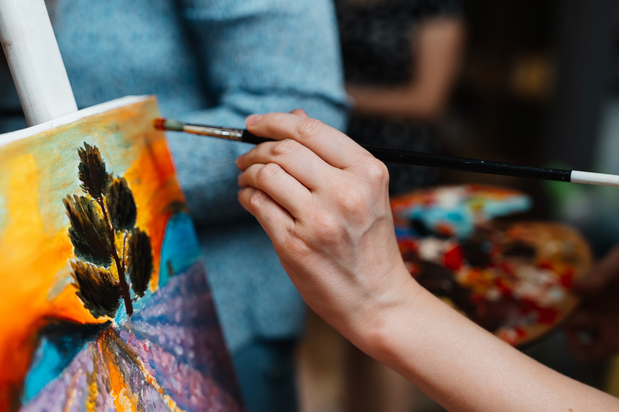 Artist painting a colorful landscape with a tree in a creative workshop